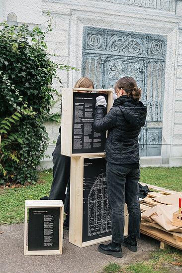 Zwei Personen die Schilder vor einem alten Gebäude aufbauen