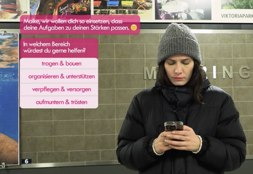 Person die in einer U-Bahn-Haltestelle auf ihr Smartphone schaut, links neben ihr sind die Texte Smartphone-App "Wo möchtest du helfen? ..." eingebeldent.
